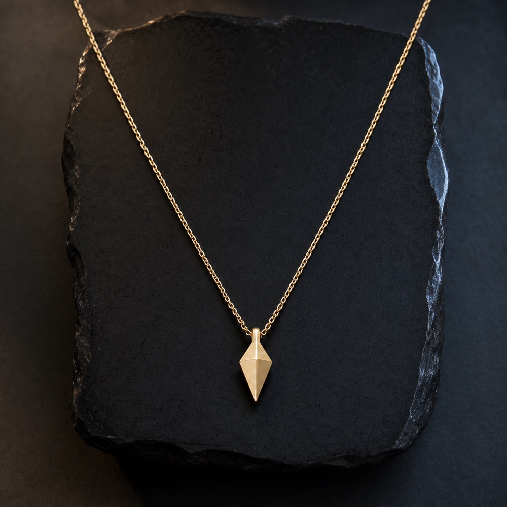 Fine gold chain with an angular pendant arranged over a black obsidian slab