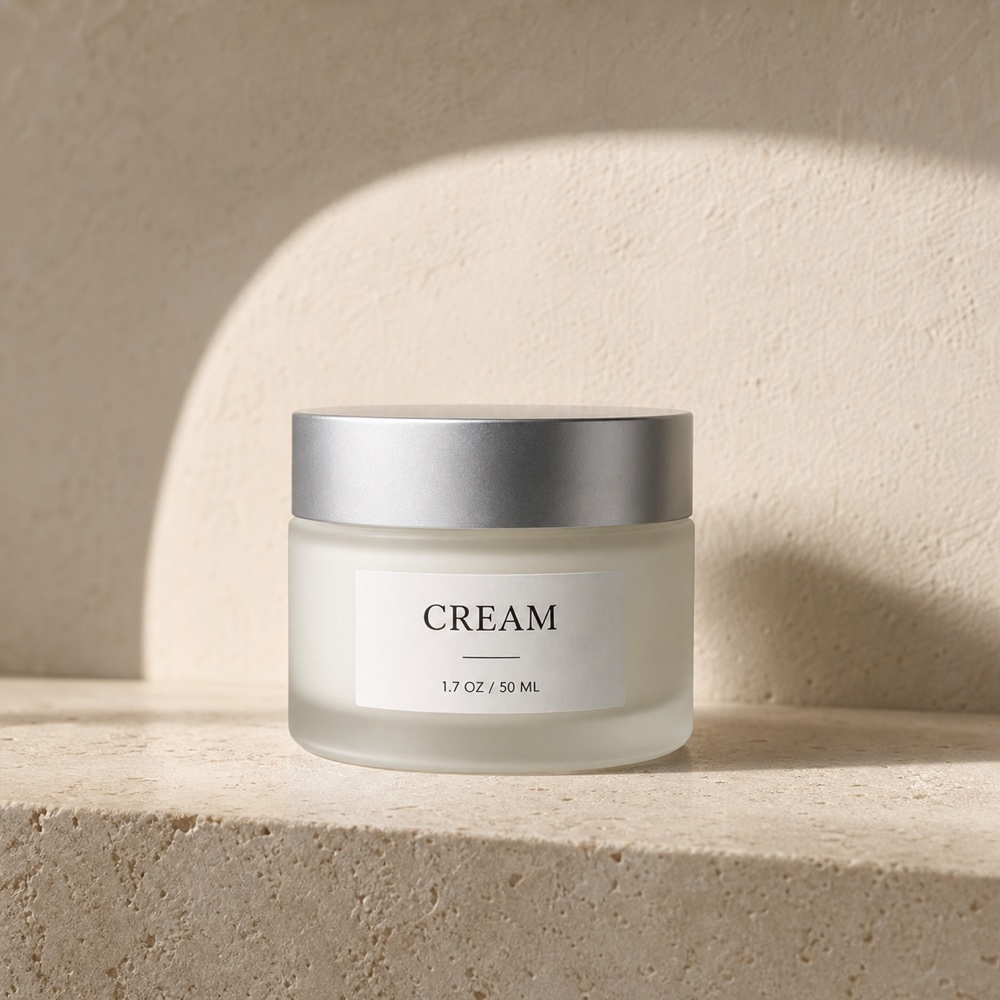 Frosted cream jar with a silver lid on warm travertine